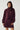 Modell med Noella N-Melda Dress Maroon, en dyp vinrød minikjole med høy hals, lange voluminøse ermer, markert midje og lett utsvingt skjørt.