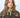 Modell med Small Triangle Scarf Green fra Sui Ava – lite salviegrønt trekantskjerf knyttet rundt halsen og stylet med brun kåpe.
