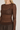 Modell med A-View Evalla Blouse Dark Brown – mørkebrun figurnær blondetopp med rund hals, lange ermer og transparent blondemønster.