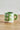 Millie Espresso Cup Green Flowers 110 ml fra Bloomingville MINI – grønn espressokopp med håndmalte hvite og rosa blomster, stylet på trebord.