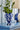 Amara Vase Blue fra Creative Collection by Bloomingville stylet med grønne grener på et blått bord – håndmalt vase i blått steintøy med hvite blomster.