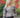 Modell utendørs med A-View Brocade Jacket – kort, figursydd jakke i brokadestoff med et detaljert blomstermønster i rosa, lyseblått, beige og sort. Jakken har V-utringning, lange ermer, markert midje og fire dekorative sølvfargede knapper foran. Stylet med mørkebrune dressbukser med beltedetalj.