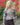 Modell utendørs med A-View Brocade Jacket – kort, figursydd jakke i brokadestoff med et detaljert blomstermønster i rosa, lyseblått, beige og sort. Jakken har V-utringning, lange ermer, markert midje og fire dekorative sølvfargede knapper foran. Stylet med mørkebrune dressbukser med beltedetalj.