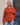 Modell med BOII Adanne Polo Knit Orange Stripe – oransje stripete strikkegenser med mørkebrune og lyse striper, klassisk polokrage, tre hvite knapper, senkede skuldre og lange ermer. Genseren har en avslappet passform og er stylet med lyseblå jeans.