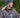Modell utendørs med MSCH Copenhagen Hope Icon Beanie i melert blå, en myk strikkelue med bred oppbrettet kant og hvit logolapp foran. Luen er stylet med matchende blå strikkevotter og en brun, quiltet jakke. Modellen holder en blå keramikkopp mellom hendene.