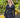 Modell i A-View Carrie Dress Black – sort omslagskjole med lett glans, V-formet utringning, lange ermer og knytebelte i midjen. Kjolen har et asymmetrisk skjørt med dekorative volanger nederst og er stylet med en sort paljettveske.