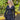 Modell i A-View Carrie Dress Black – sort omslagskjole med lett glans, V-formet utringning, lange ermer og knytebelte i midjen. Kjolen har et asymmetrisk skjørt med dekorative volanger nederst og er stylet med en sort paljettveske.