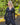 Modell i A-View Carrie Dress Black – sort omslagskjole med lett glans, V-formet utringning, lange ermer og knytebelte i midjen. Kjolen har et asymmetrisk skjørt med dekorative volanger nederst og er stylet med en sort paljettveske.